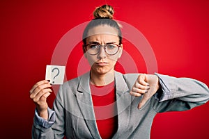 Young beautiful blonde woman with blue eyes holding reminder paper with question mark with angry face, negative sign showing