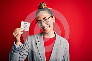 Young beautiful blonde woman with blue eyes holding reminder paper with question mark with a happy face standing and smiling with