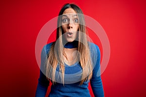 Young beautiful blonde woman with blue eyes standing over red background afraid and shocked with surprise expression, fear and