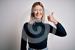 Young beautiful blonde woman with blue eyes standing over white isolated background doing happy thumbs up gesture with hand