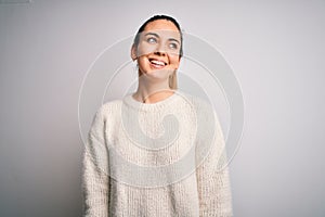 Young beautiful blonde woman with blue eyes wearing casual sweater over white background looking away to side with smile on face,