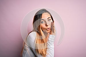 Young beautiful blonde woman with blue eyes wearing white t-shirt over pink background hand on mouth telling secret rumor,