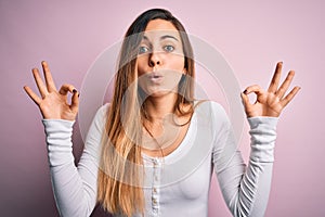 Young beautiful blonde woman with blue eyes wearing white t-shirt over pink background looking surprised and shocked doing ok