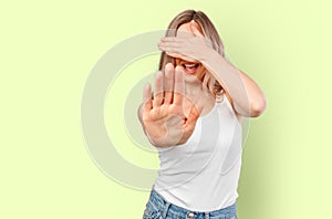 Young beautiful blonde woman covering eyes with hands and doing stop gesture isolated on color background.