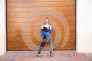 young and beautiful blonde woman dressed in black t-shirt and blue leather jacket and jeans on wooden background poses for photos