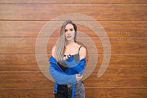 young and beautiful blonde woman dressed in black t-shirt and blue leather jacket and jeans on wooden background poses for photos