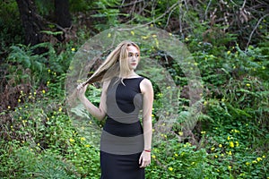 Young, beautiful blonde woman dressed in black walks through the forest in different postures and expressions. In the background