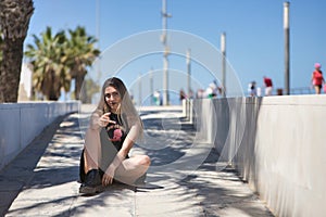 Young, beautiful blonde woman, green eyes, with black top and skirt, tattoos, sitting on the floor, looking at the camera,