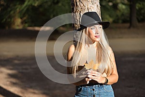 Young, beautiful, blonde woman with green eyes and hat, holding a dry leaf in her hands with melancholic look. Concept looks,