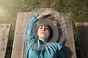 Young, beautiful, blonde woman in green shirt, eyes closed lying on a wooden table sunbathing. Concept peace, tranquility, beauty