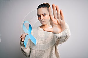 Young beautiful blonde woman holding blue cancer ribbon over isolated white background with open hand doing stop sign with serious