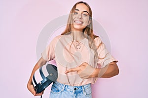 Young beautiful blonde woman holding motorcycle helmet smiling happy pointing with hand and finger