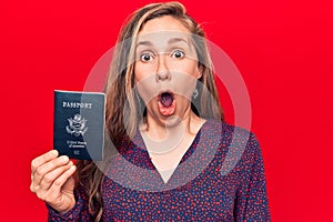 Young beautiful blonde woman holding passport of united states of america scared and amazed with open mouth for surprise,