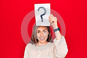 Young beautiful blonde woman holding question mark over head looking positive and happy standing and smiling with a confident