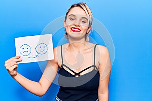 Young beautiful blonde woman holding sad to happy emotion paper looking positive and happy standing and smiling with a confident