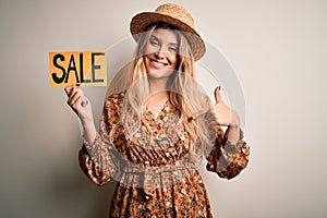 Young beautiful blonde woman holding sale banner over isolated white background with surprise face pointing finger to himself