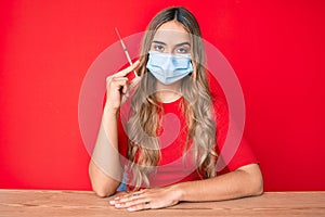 Young beautiful blonde woman holding syringe thinking attitude and sober expression looking self confident