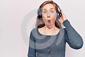 Young beautiful blonde woman listening to music wearing headphones scared and amazed with open mouth for surprise, disbelief face