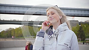 A young beautiful blonde woman listens to music on her smartphone using headphones. A young woman enjoys a walk along