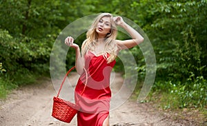 Young, beautiful blonde woman with long hair in a red dress posing with an apple in one hand and a basket in the other hand