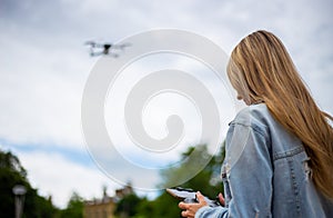 Young beautiful blonde woman piloting a drone holding a remote control