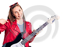 Young beautiful blonde woman playing electric guitar pointing finger to one self smiling happy and proud