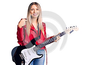 Young beautiful blonde woman playing electric guitar pointing finger to one self smiling happy and proud