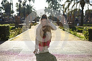 Young beautiful blonde woman with a ponytail in her hair wearing a pink skirt and fringed jacket rests one knee, one hand on the