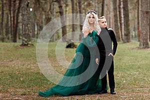 young beautiful blonde woman queen with young boy in black outfit. Princess mother walks with son. autumn green forest