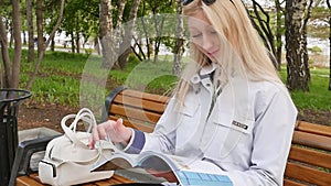A young beautiful blonde woman is reading a magazine and is resting on a park bench. A student learns English during a