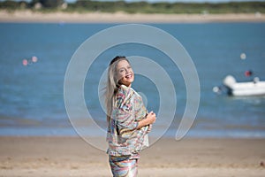Young beautiful blonde woman on the seashore having fun making different expressions and touching her hair. In the background on