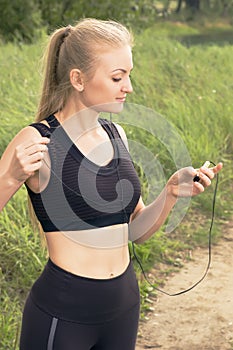 Young beautiful blonde woman setting music on player before morning run outdoors