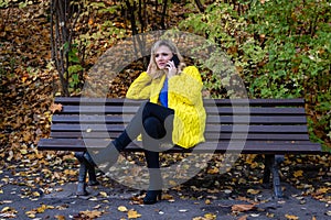 Young, beautiful, blonde woman sits on a bench in the park and talking on the phone