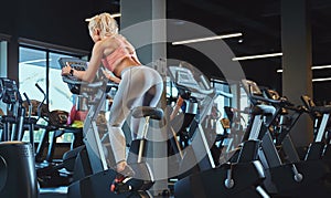 Young beautiful blonde woman in sportswear training on an exercise bike in modern fitness center.