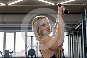 Young beautiful blonde woman trains in the gym. Pulldown exercise. Back muscle training