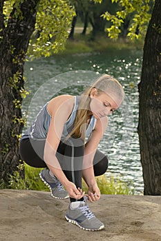 Young beautiful blonde woman tying sport shoe laces outdoors