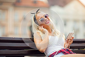 Young beautiful blonde woman using phone sitting on a bench