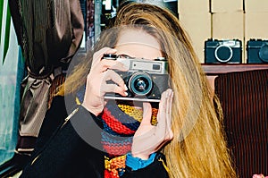 Young beautiful blonde woman with a vintage camera takes pictures in a cafe. Winter portraits of the photographer