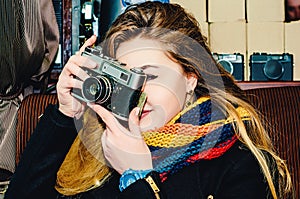 Young beautiful blonde woman with a vintage camera takes pictures in a cafe. Winter portraits of the photographer