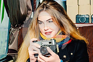 Young beautiful blonde woman with a vintage camera takes pictures in a cafe. Winter portraits of the photographer