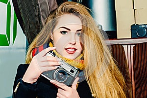 Young beautiful blonde woman with a vintage camera takes pictures in a cafe. Winter portraits of the photographer