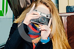 Young beautiful blonde woman with a vintage camera takes pictures in a cafe. Winter portraits of the photographer