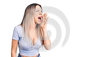 Young beautiful blonde woman wearing casual clothes shouting and screaming loud to side with hand on mouth