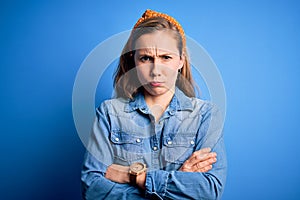 Young beautiful blonde woman wearing casual denim shirt and diadem over blue background skeptic and nervous, disapproving