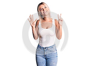 Young beautiful blonde woman wearing casual sleeveless t-shirt showing and pointing up with fingers number seven while smiling