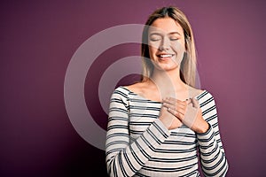 Young beautiful blonde woman wearing casual striped shirt over purple isolated background smiling with hands on chest with closed