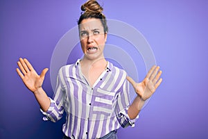 Young beautiful blonde woman wearing casual striped shirt standing over purple background crazy and mad shouting and yelling with