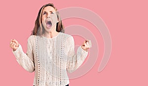 Young beautiful blonde woman wearing casual sweater crazy and mad shouting and yelling with aggressive expression and arms raised