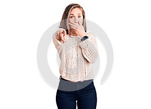 Young beautiful blonde woman wearing casual sweater laughing at you, pointing finger to the camera with hand over mouth, shame