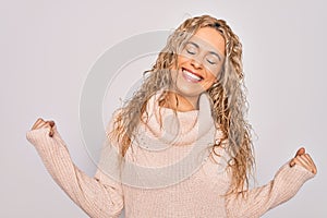 Young beautiful blonde woman wearing casual sweater standing over isolated white background very happy and excited doing winner